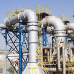 Industrial processing plant with large metal pipelines and steel framework.